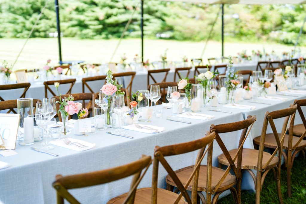 Long tables under tent set with light florals and wooden seating.