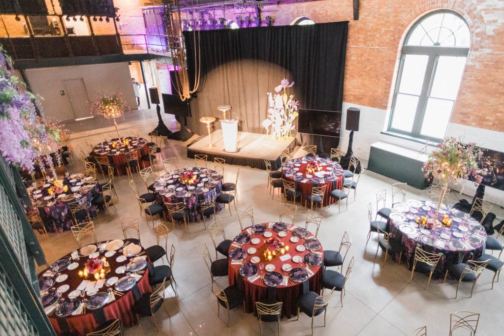 Round tables set up in the main space with a stage and purple uplighting at The Stack at Municipal Light Plant.